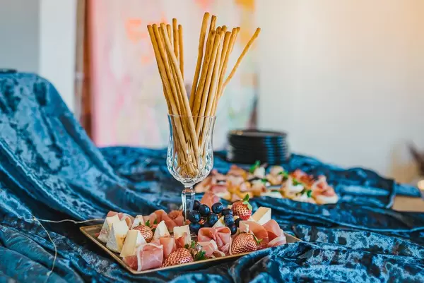 Table Filled With Cheese, Berries,  Prosciutto And Bread Sticks