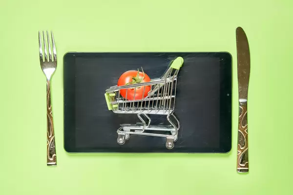 Tablet with shopping cart, spoon and fork on green