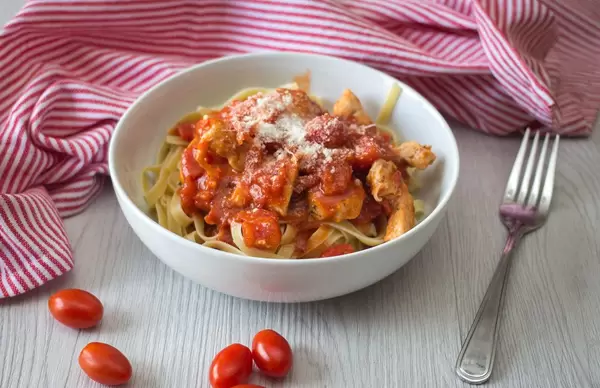 Tagliatelle Nudeln mit Hühnchen in Tomatensoße und Parmezan in einer Schüssel vor einem Küchentuch