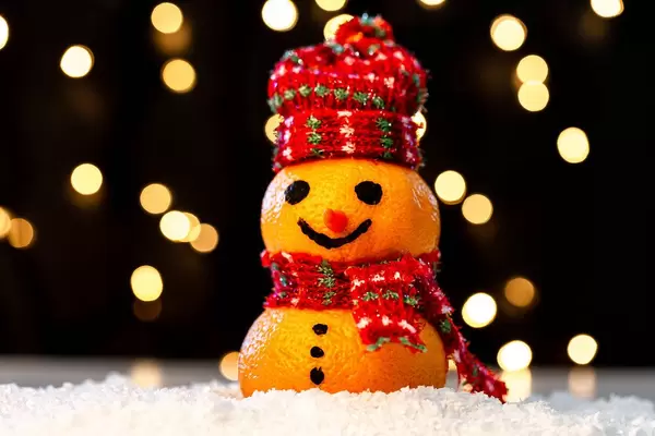 Tangerine snowman in the snow on a blurry background of luminous garlands (Flip 2019)