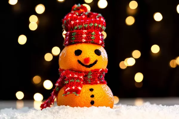 Tangerine snowman in the snow on a blurry background of luminous garlands