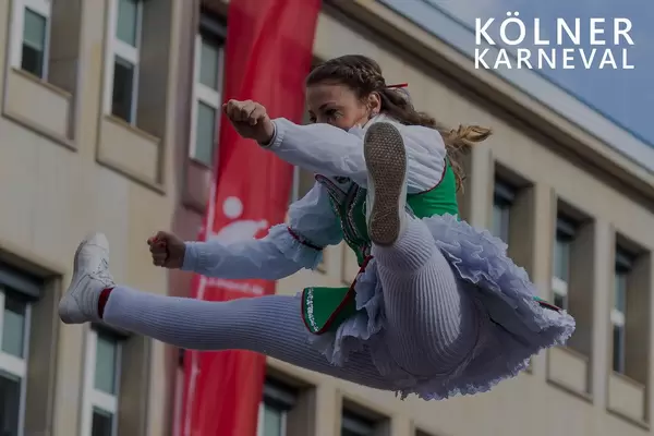 Tanzmariechen im Kostüm, macht einen Spagatsprung in der Luft, neben dem Bildtitel "Kölner Karneval"