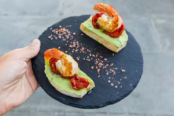 Tapas at Q11, Pollença: toasted bread, king prawns, dried tomatoes, avocado cream on a round board