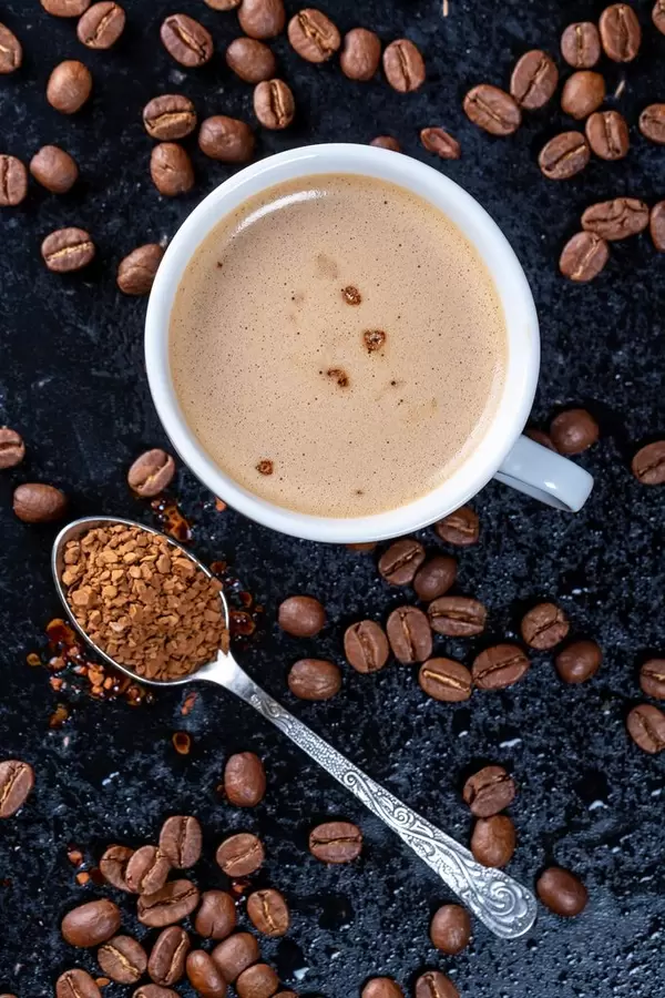 Tasse mit gemahlenem Kaffee, geraspeltem Kaffee auf einem Löffel und Kaffeebohnen auf schwarzem Untergrund aus der Vogelperspektive