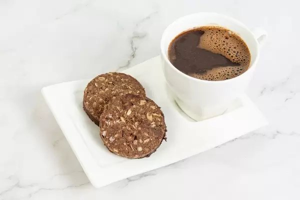 Tasse mit schwarzem Kaffee, neben zwei Schokoladen-Erdnusskeksen