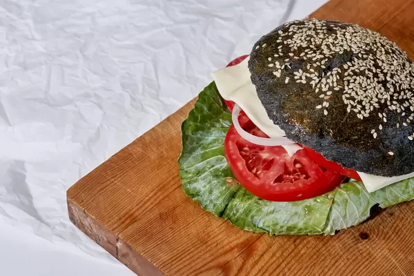 Tasty black burger with chicken meat, cheese and tomato slices on the cutting background