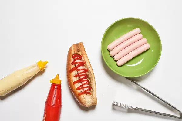 Tasty hotdog, sausages, mustard and mayonnaise on white surface, overhead view