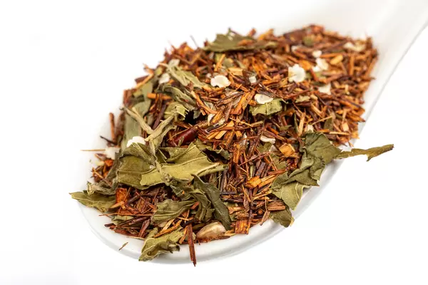 Tea with dried sprigs and green tea leaves in a white spoon