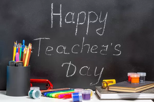 Teacher books and a stand with pencils on the table, on the background of a blackboard with chalk. The concept of the teacher's day