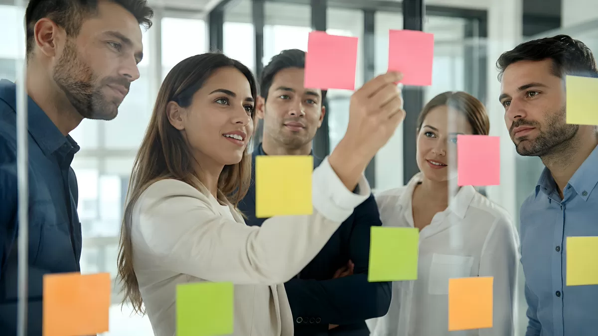 Team klebt bunte Haftnotizen an Glaswand im Büro