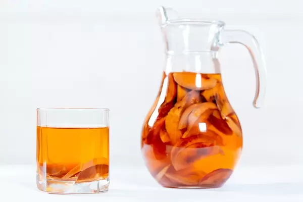 Tee aus getrockneten Früchten in Krug und Glas vor weißem Hintergrund