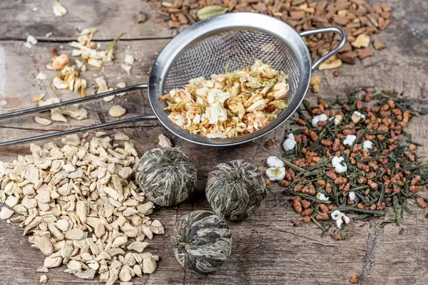 Tee-Hintergrund mit verschiedenen Teesorten und einem Sieb auf einem hölzernen Tisch