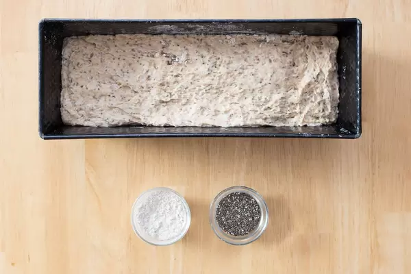 Teig für Chia-Brot in der Form sowie Mehl und Chia-Samen in kleinen Glasschüsseln