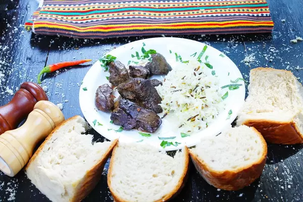 Teller mit Entenleber und Wildreis, mit Brot serviert. Schwarzer hölzerner Tisch