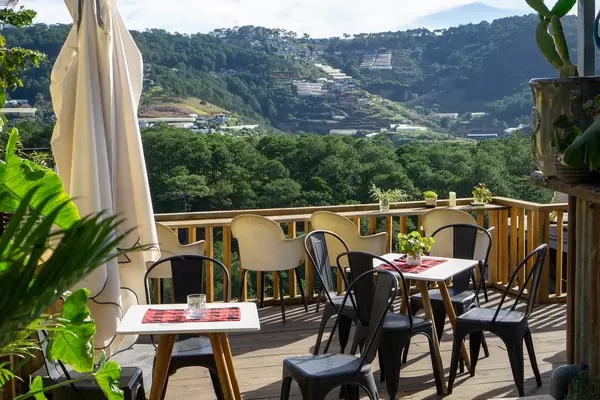 Terrace with Tables, Chairs and Sun Umbrella of an Outdoor Cafe with a View of Mountains and Grow Houses in Da Lat, Vietnam