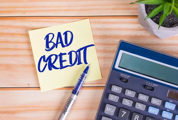 Text Bad Credit auf einer Haftnotiz mit Kugelschreiber, Taschenrechner und Tischpflanze auf einem Holztisch