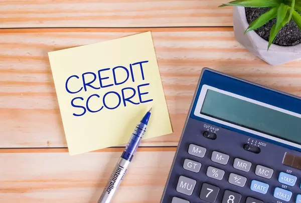 Text Credit Score auf einer Haftnotiz mit Kugelschreiber, Taschenrechner und Tischpflanze auf einem Holztisch