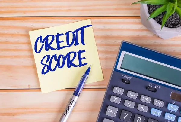 Text Credit Score auf gelber Haftnotiz mit Kugelschreiber, Taschenrechner und Tischpflanze auf einem Holztisch