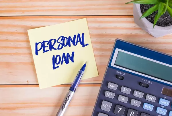 Text Personal Loan auf einer Haftnotiz mit Kugelschreiber, Taschenrechner und Tischpflanze auf einem Holztisch