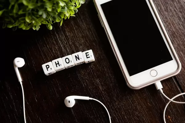 Textwürfel zeigen das Wort "Phone" - Telefon, neben einem Handy mit weißen Kopfhörern