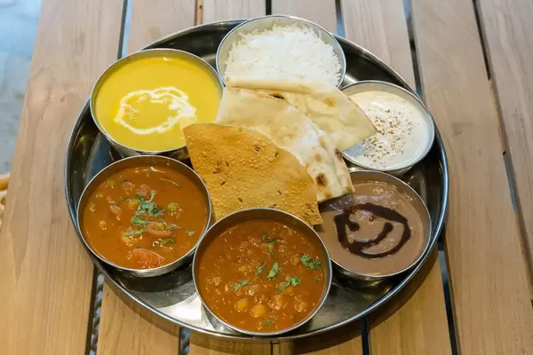 Thali Lunch - Hühnchenbrust in Kokos-Cashew-Curry serviert mit Basmati Reis, Fladenbrot, Kartoffel-Tomaten-Curry, Kichererbsen-Curry, Raita und Schokoladencreme