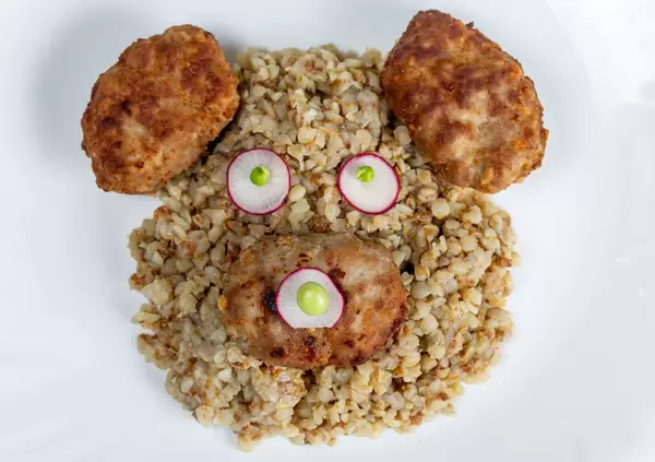 The concept of a children's lunch. The face of a bear made of buckwheat porridge, cutlets and radishes