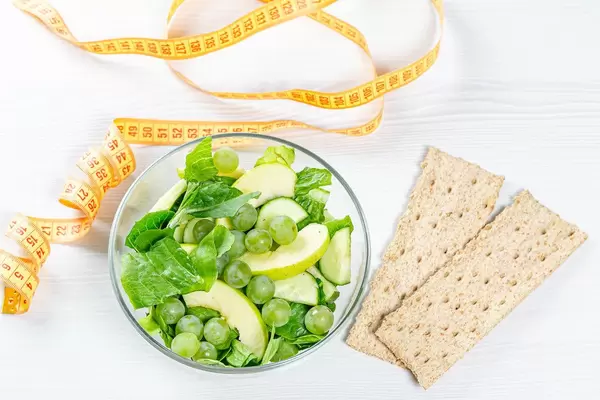 The concept of a diet dinner. Fresh fruit and vegetable salad with wheat germ loaves and measuring tape