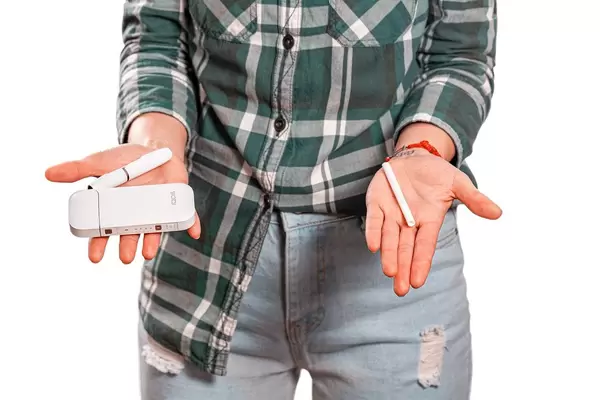 The concept of bad habits. A woman holds a cigarette in one hand and IQOS in the other