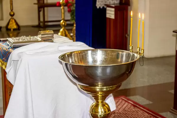 The concept of child baptism in the Christian Church. A bowl of water for the baptism of the child and burning candles (Flip 2019)