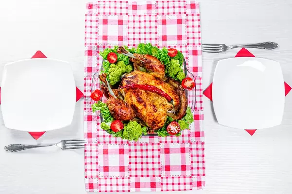 The concept of dinner for two. Baked chicken with vegetables and Cutlery on the table