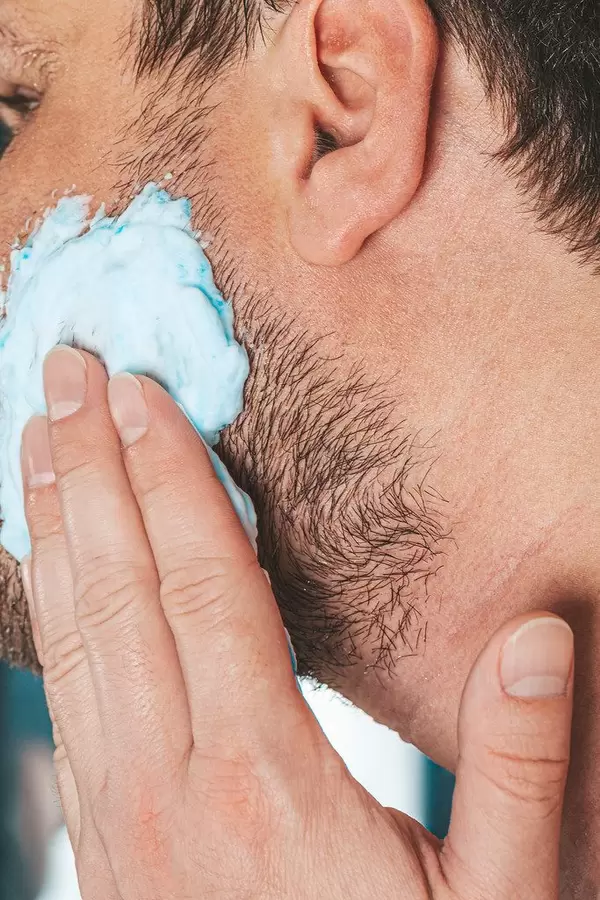 The concept of facial care for men. A man applies shaving gel to his face