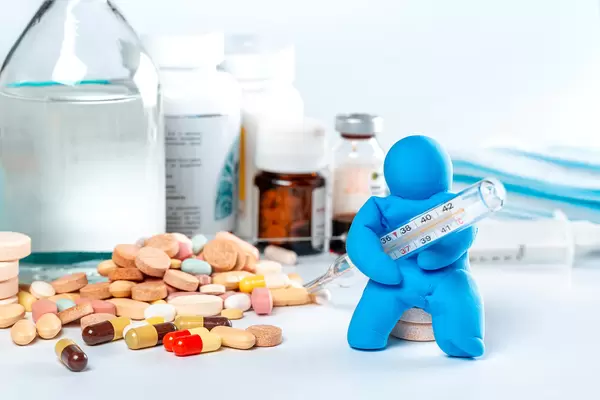 The concept of health care, diagnosis, prevention and treatment. Human model with a thermometer in his hands and medicines