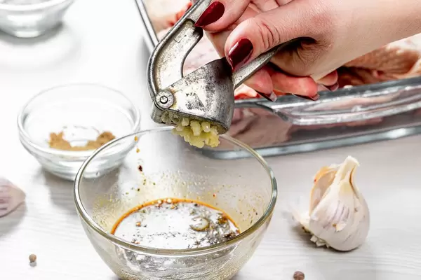 The cook squeezes the garlic with a garlic grinder into the marinade sauce