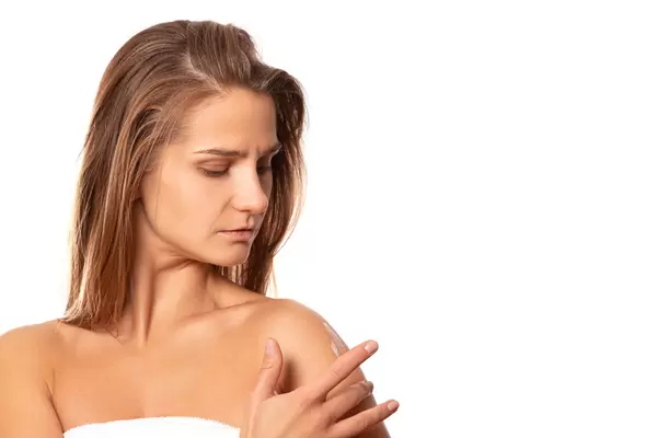 The girl applies a moisturizer to the skin of the shoulder