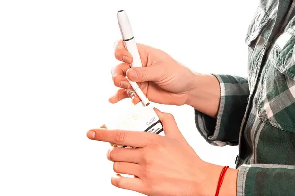 The girl holds in her hand a heating electronic cigarette with a tobacco stick for smoking