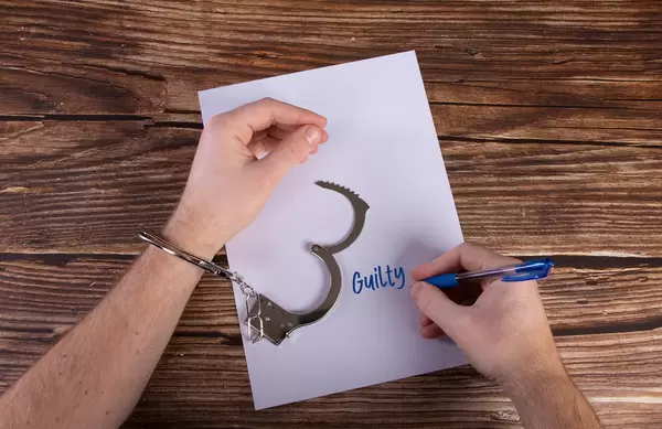 The hands of the criminal in handcuffs writting Guilty on a paper