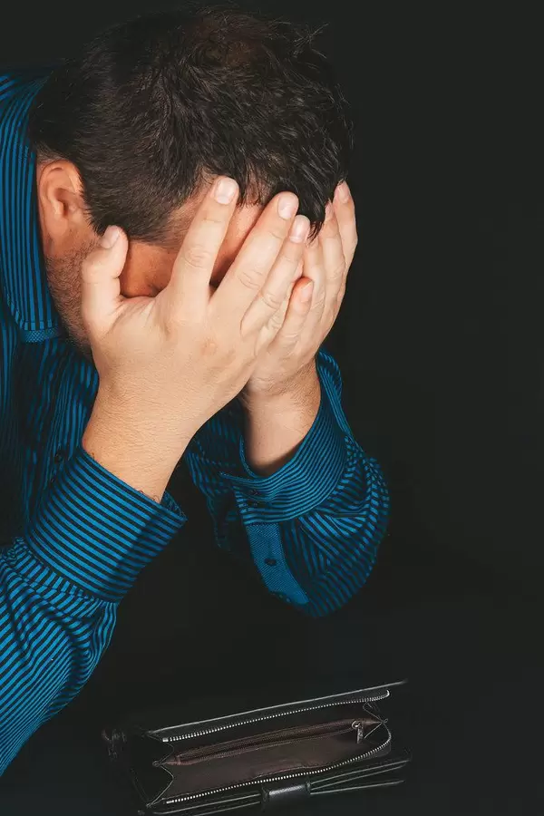 The man covered his face with his hands on a dark background with an empty wallet. Bankrupt, financial problems concept