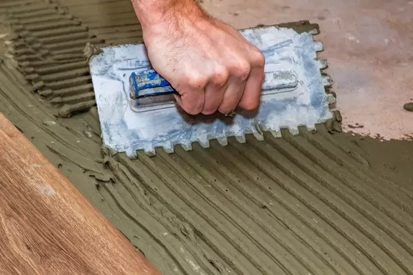 The man levels the adhesive mixture on the floor