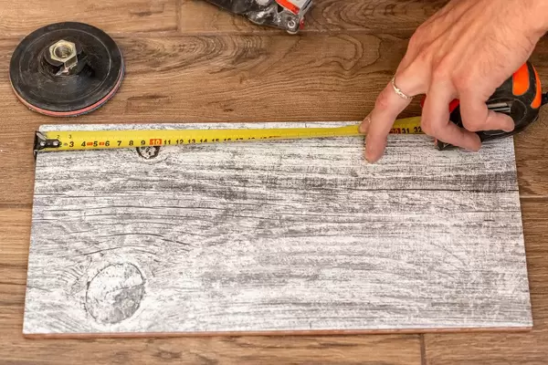 The master uses a tape measure to measure the dimensions on the tile
