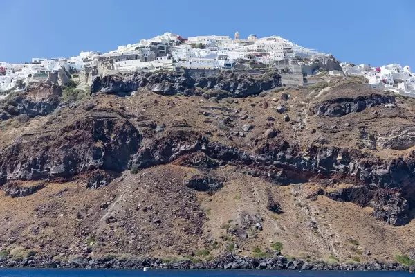 The picturesque village of Oia sits on layers of volcanic ground, seen from the sea during a boat trip