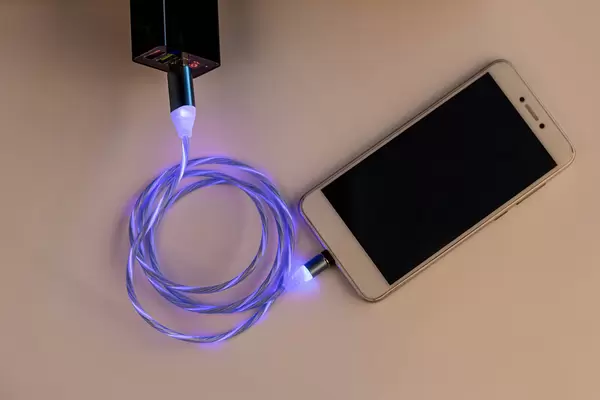 The smartphone is connected to a charger with a glowing cable