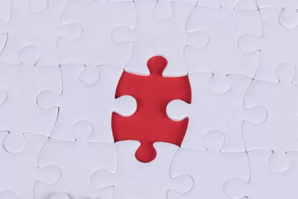 The texture of a white jigsaw puzzle in an assembled state with one missing element forming a red space