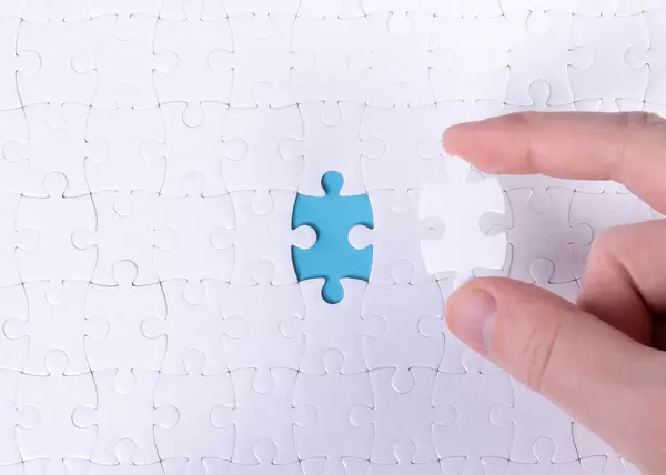 The texture of a white jigsaw puzzle in the assembled state with one missing element that the male hand puts in