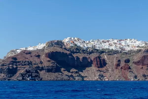 The volcanic cliffs of Santorini with the Aegean sea and the white village of Oia seen from a boat