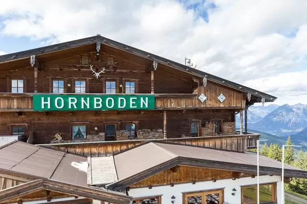 The wooden building of mountain restaurant Hornboden with its green sign and horns as a symbol