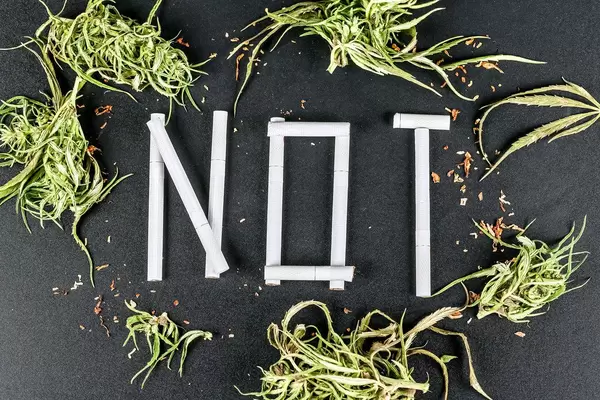 The word NOT made of cigarettes on a black background with hemp leaves, top view