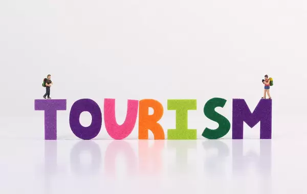 The word Tourism with tiny travelers on white background