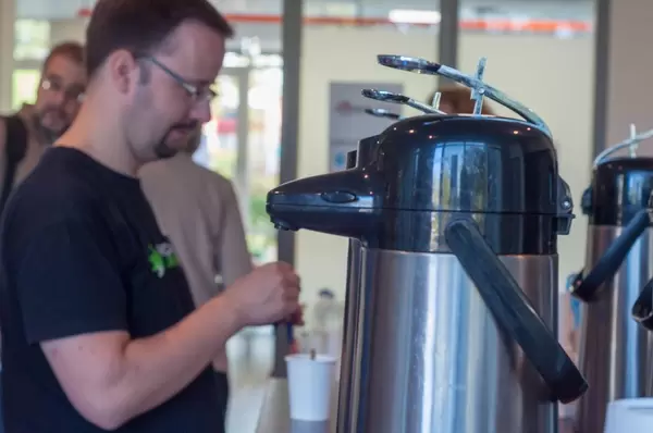 Thermoskanne‎n mit Kaffee und Tee und Teilnehmer mit Bechern im verschwommenen Hintergrund