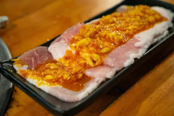 Thin Raw Pork Slices topped with Sauce and Garlic on a Black Ceramic Plate at a Barbecue Restaurant