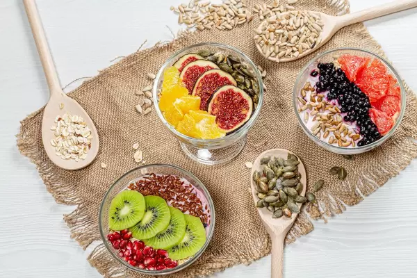 Three bowls of oatmeal with fresh fruit and seeds on a burlap background with wooden spoons (Flip 2019)